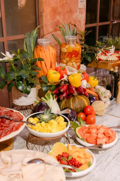 Wedding antipasto table with wedding charcuterie table spreads of cheese, prosciutto, fruit bowls, citrus jars on wooden risers by stone wall