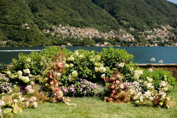 Wedding ceremony flowers with ceremony ground florals of hydrangeas, roses, and wildflowers on a lakeside lawn with mountains beyond