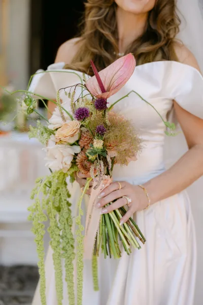 Bridal bouquet, tropical bridal bouquet with pink anthurium and trailing greenery, tied with blush ribbon in front of a sunlit doorway