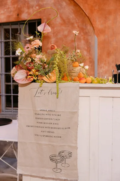 Wedding bar decor with a wedding bar menu sign, floral centerpiece, and citrus garnishes on a white bar against a stucco wall arch