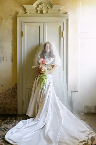 Bridal portrait of a bride holding bouquet with anthurium and orchids, veil and long train by vintage doors in soft window light
