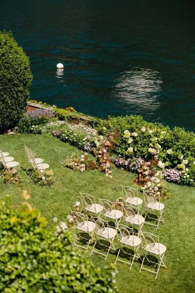Ceremony setup with outdoor ceremony seating of white metal chairs and hydrangea floral arrangements on a lawn by the waterfront