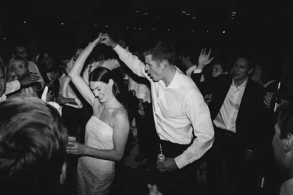 Reception dance with a couple dancing as the bride twirls, clutching a cocktail glass under glowing ceiling lights on the indoor dance floor.