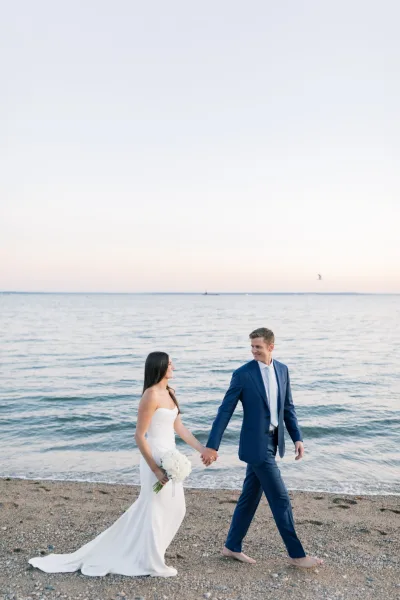 Couple portrait for beach wedding photos as the bride holds a white bouquet beside the groom on a sandy shore with ocean and sky.