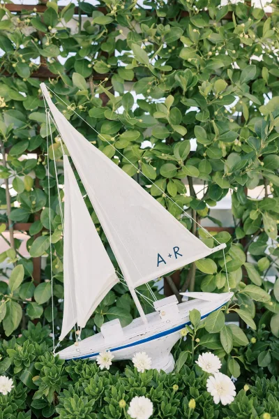Sailboat wedding decor as a nautical wedding detail: a white sailboat prop with a monogrammed sail before garden foliage and a wooden trellis.