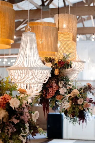 Reception lighting decor with hanging chandeliers and pampas grass floral installation beneath wood beams and skylights in an indoor venue ceiling