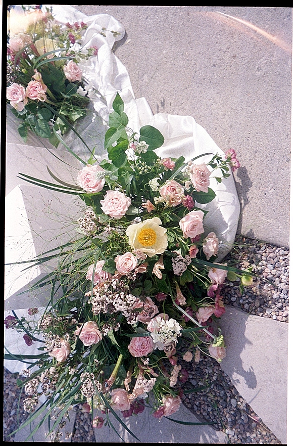 Bridal bouquet with pink roses, greenery, and baby's breath, tied with a silk ribbon and veil trailing on stone pavement