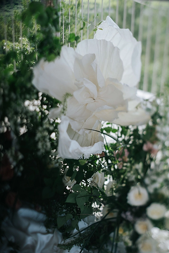 Wedding floral installation with a ceremony floral arrangement of white flowers and lush greenery draped over a railing with garden foliage behind