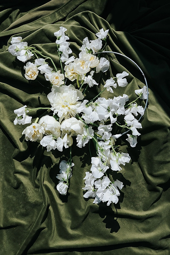Bridal bouquet with white wedding bouquet blooms and greenery stems, finished with a silver hoop handle against olive green draped fabric