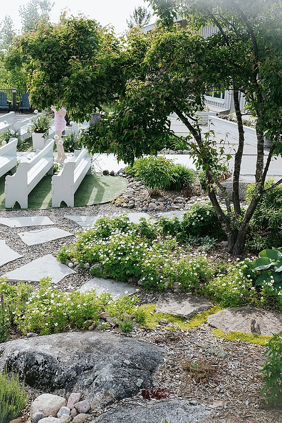 Outdoor ceremony setup with backyard wedding ceremony seating, white benches lining an aisle runner through a landscaped garden path