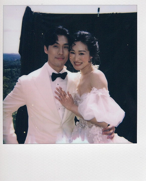 Couple portrait in polaroid wedding photo style, bride in puff sleeve gown hugging groom in white tuxedo with black bow tie outdoors
