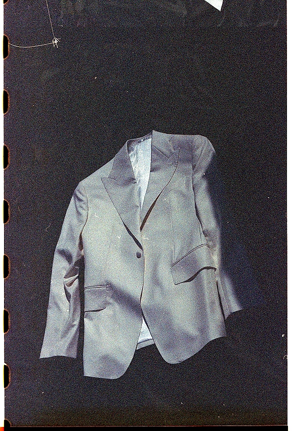 Groom suit jacket in a wedding suit flat lay, showing notch lapel, single button, pocket flap, and lining against a dark backdrop
