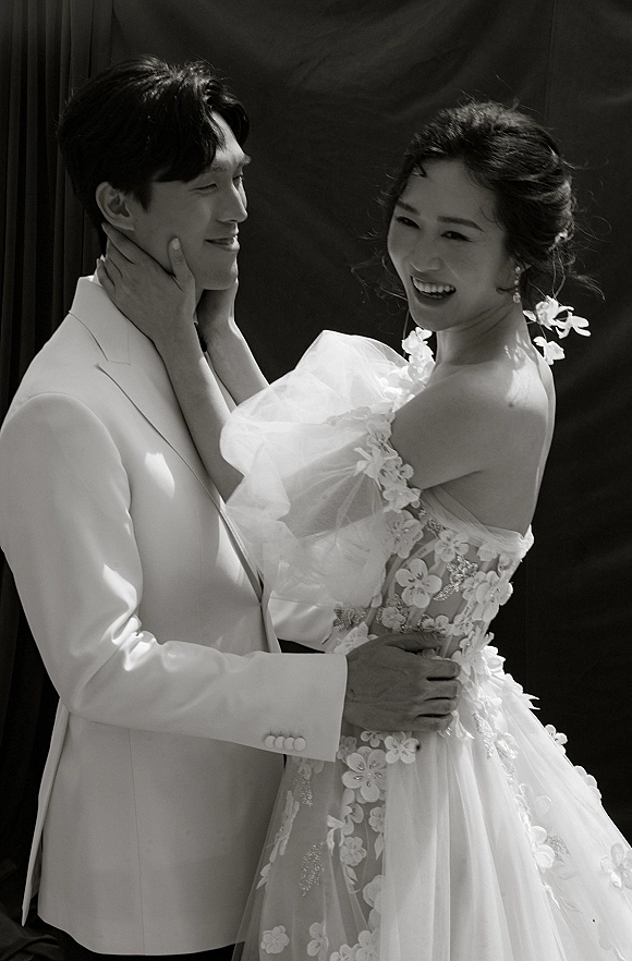 Couple portrait of a bride touching the groom’s face, her floral appliqué wedding dress with tulle sleeves against a dark studio backdrop