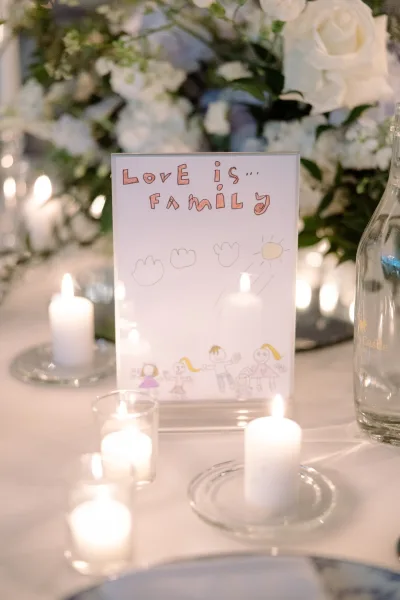 Wedding signage presented as a refined table sign idea in an acrylic sign holder, set amid a white tablecloth with nearby glassware.