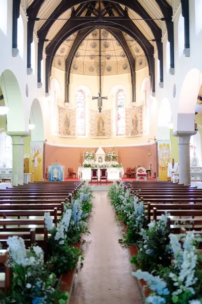 Ceremony aisle design featuring church aisle flowers flanking the path, pews lining the way beneath vaulted arches and stained glass windows.