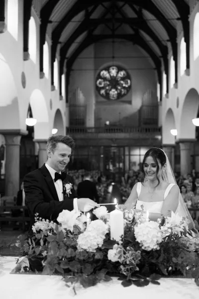 Unity candle ceremony at a church wedding ceremony as the bride and groom light tapers, her veil catching candlelight beneath stained glass arches
