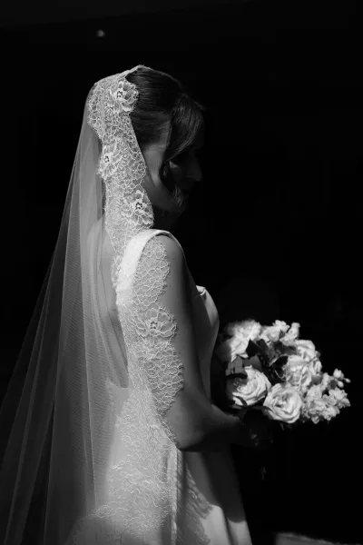 Bridal portrait of a bride with lace veil framing her face, her gaze serene as delicate lace drapes softly, evoking a timeless, romantic elegance.