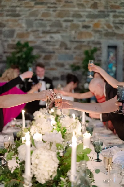 Wedding toast as wedding guests toast with raised champagne flutes before a stone wall and stained glass window