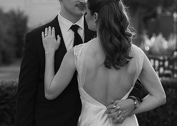Couple portrait in a black and white wedding portrait, bride and groom embrace with her hand on his chest in a garden setting