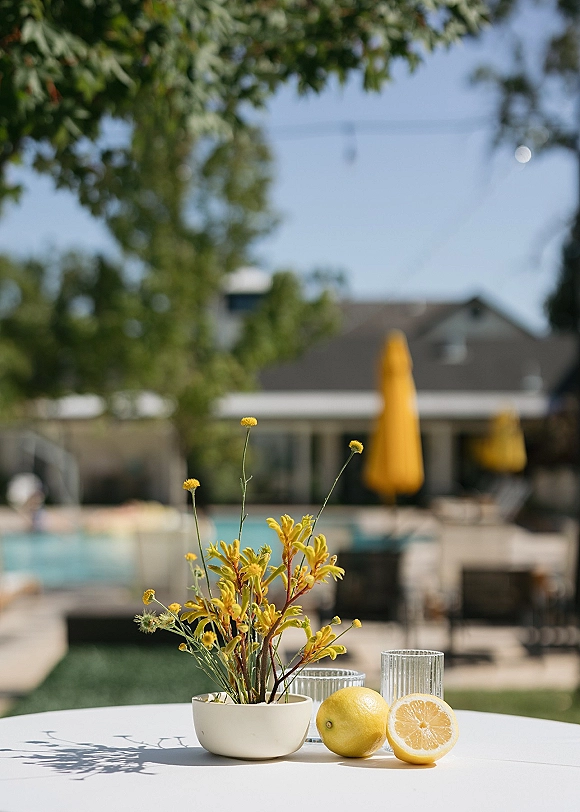 Wedding tablescape with lemon wedding centerpiece, yellow wildflowers in bud vases on a white round table by a sunny poolside patio