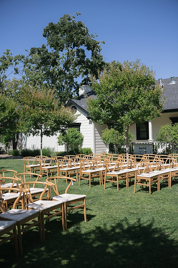Ceremony seating with outdoor wedding ceremony chairs in neat rows, wood chairs with white cushions and programs on a green lawn near trees
