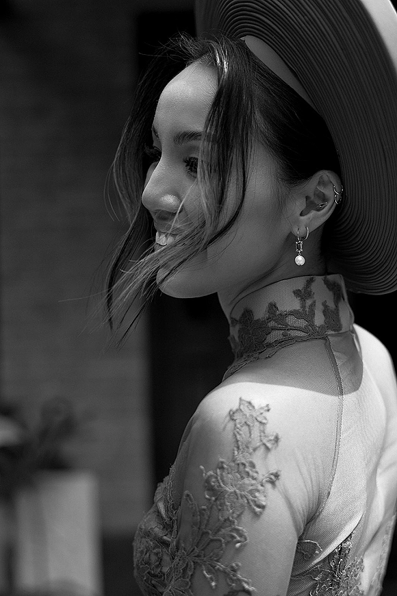 Bridal portrait in black and white of a bride in side profile looking over her shoulder, wearing a wide brim hat in a blurred indoor venue