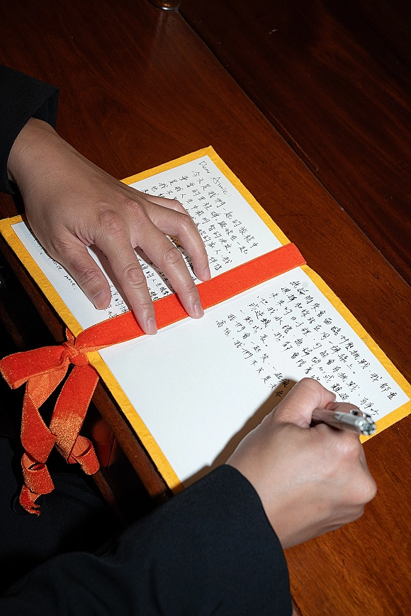 Wedding vows in a vow book with ribbon, handwritten calligraphy on paper beside a pen on a rustic wood table