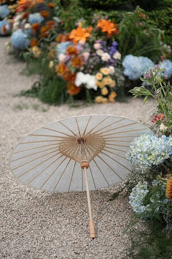 Wedding parasol with bridal parasol accessory placed beside hydrangeas and greenery on a gravel path in a garden setting