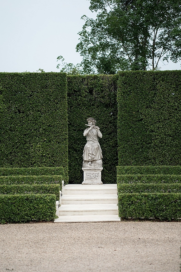 Garden statue backdrop with a stone statue on a pedestal, framed by trimmed hedges and steps in a formal garden with gravel path