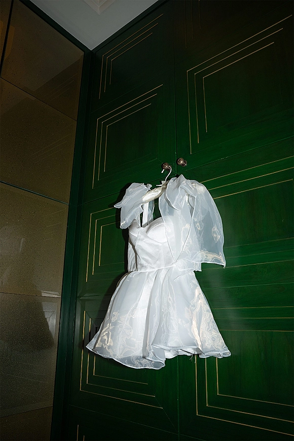Wedding dress, short wedding dress on a hanger with strapless satin bodice, tulle overlay, and lace hem against green paneled doors