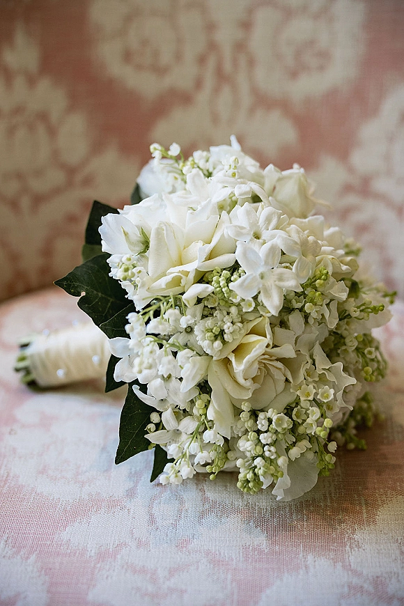 Wedding bouquet of white flowers with ivy leaves on patterned upholstery, hand-tied with an ivory wrap for a classic look
