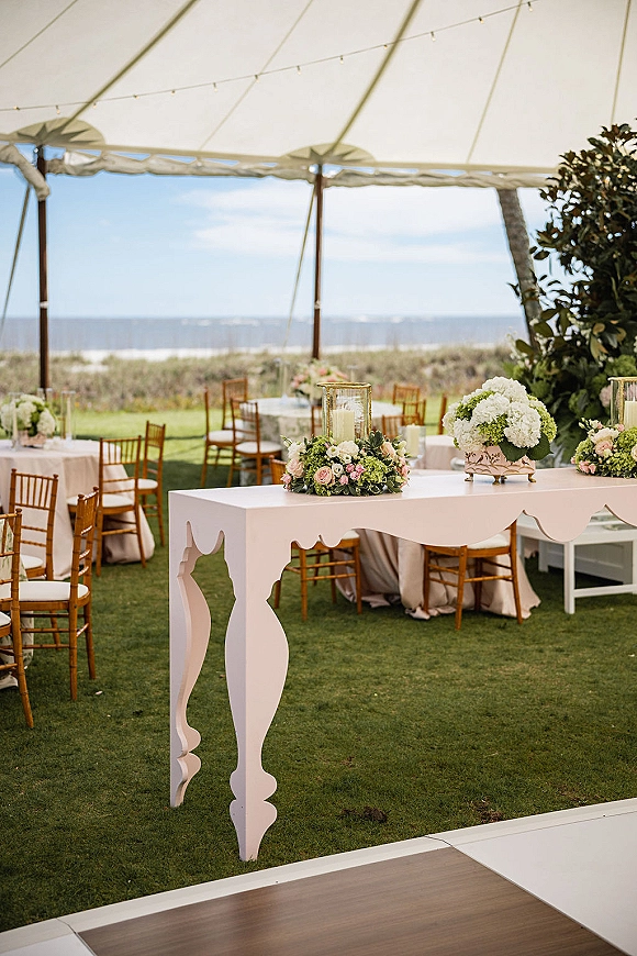 Wedding reception decor with hydrangea and rose centerpieces and hurricane candle on a white display table under a tent by the ocean view