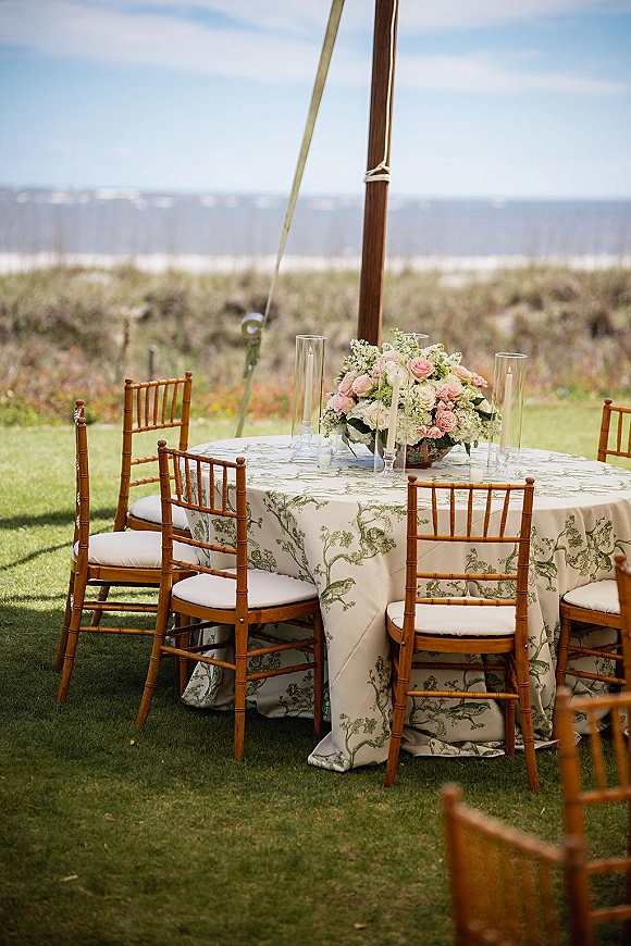 Reception tablescape on a round wedding reception table with rose and hydrangea centerpiece and taper candles under a tent by ocean dunes