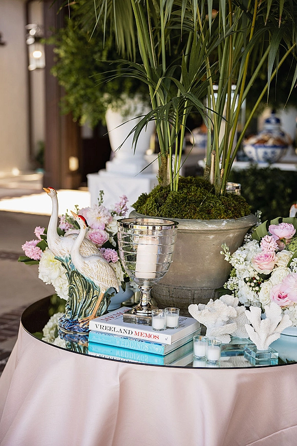 Wedding tabletop decor with cocktail table decor on a mirrored round table, blush linen, pink roses, candles, books, and palm on patio