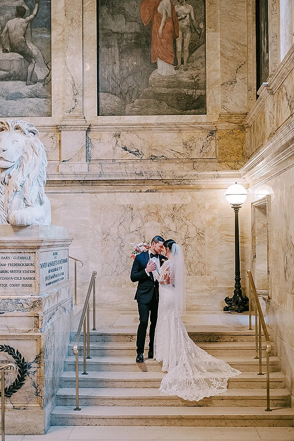 Couple portrait of bride and groom on stairs, embracing with bouquet and veil on a marble staircase with brass handrails and murals