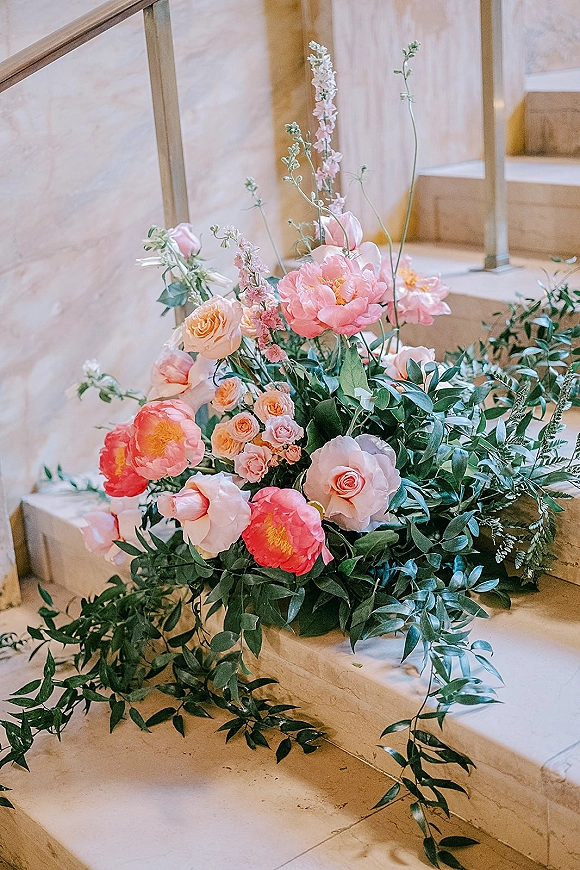 Wedding floral arrangement with pink peonies and roses draped along a stone staircase railing, with blush blooms and trailing greenery