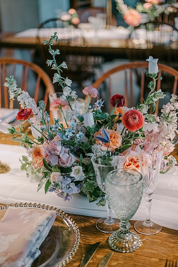 Reception tablescape with wedding table centerpiece of pastel flowers and greenery, gold flatware and green goblet on an indoor dining table