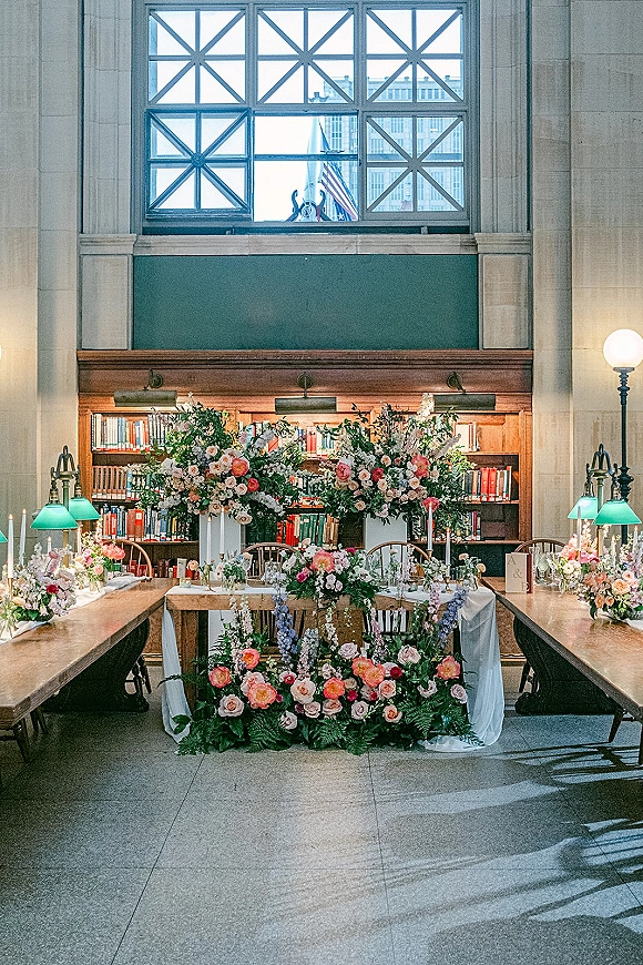 Wedding sweetheart table with sweetheart table flowers, lush roses and greenery runner, taper candles, and green banker lamps in a library setting