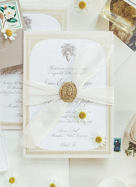 Wedding invitation suite with letterpress wedding invitations, classic calligraphy, gold border, wax seal and daisies on white fabric flat lay