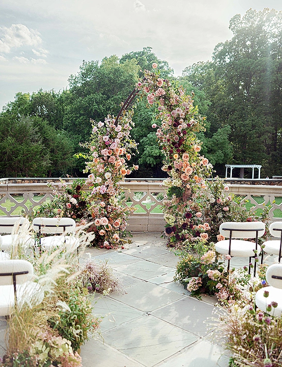 Wedding ceremony arch with a floral wedding arch of garden roses and greenery, framed by white chairs on a stone patio terrace