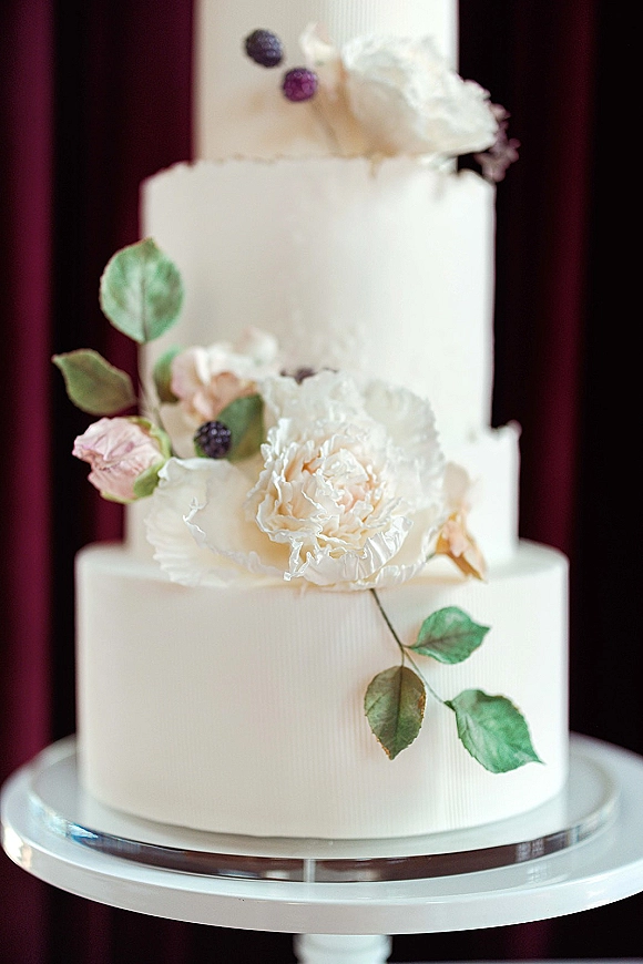 Wedding cake three tier wedding cake with smooth buttercream, sugar peony and rose florals on a stand against a dark backdrop