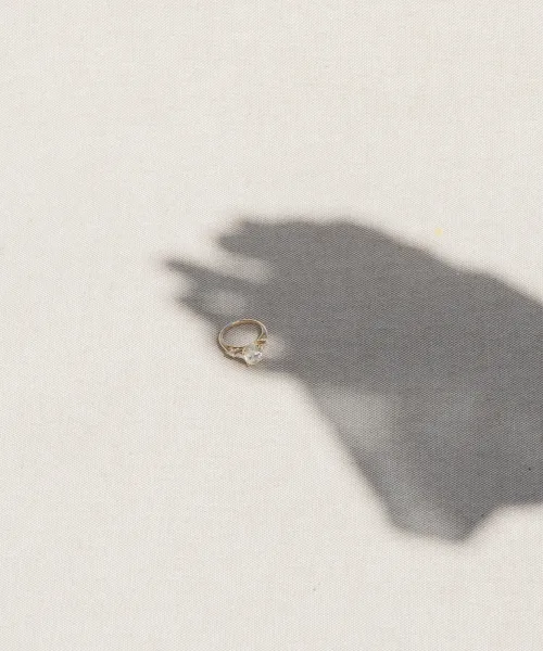 Engagement ring with a solitaire diamond on a thin gold band, resting on light fabric with a soft shadow in the background