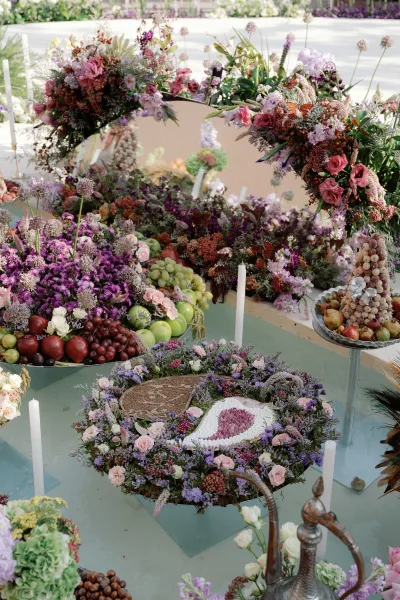 Reception tablescape with a wedding fruit centerpiece of grapes, apples, and pears beside wildflower blooms, butterfly accents, and tapered candles on an outdoor patio