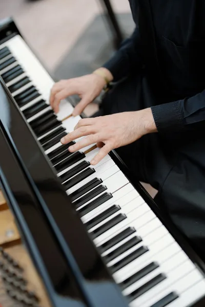 Wedding pianist playing ceremony live music on a digital keyboard, black suit sleeve and wristwatch visible above the keys indoors