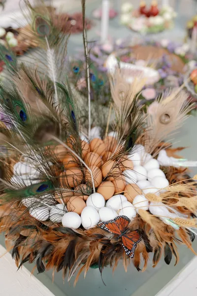 Wedding centerpiece with peacock feather centerpiece details, eggs nestled in moss on a table, with blurred floral arrangements behind
