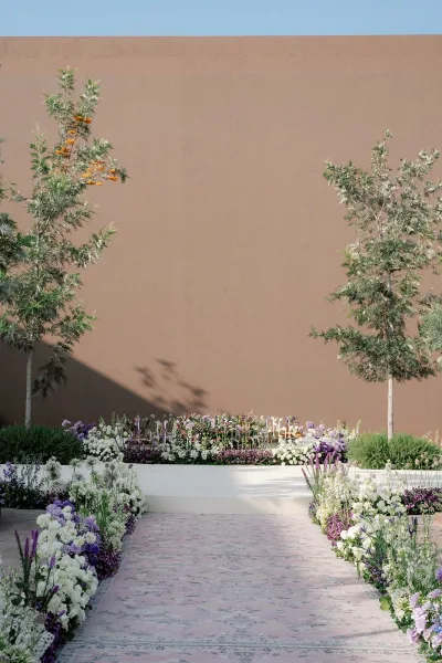 Ceremony aisle decor with wedding aisle flowers lining a patterned runner, with candles leading to a pedestal platform in a courtyard setting