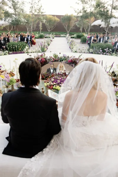 Ceremony moment as bride and groom stand at the altar, bride in long veil and dress, guests seated along a flower-lined garden aisle