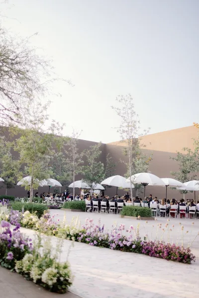 Outdoor ceremony setup with courtyard wedding ceremony seating, white parasols over rows of chairs and pastel aisle florals in a stucco courtyard