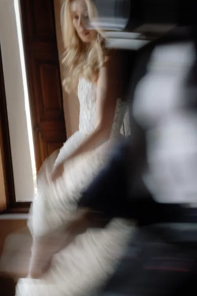 Bridal portrait of a bride getting ready in a lace wedding dress, looking down by window light near a wooden door indoors