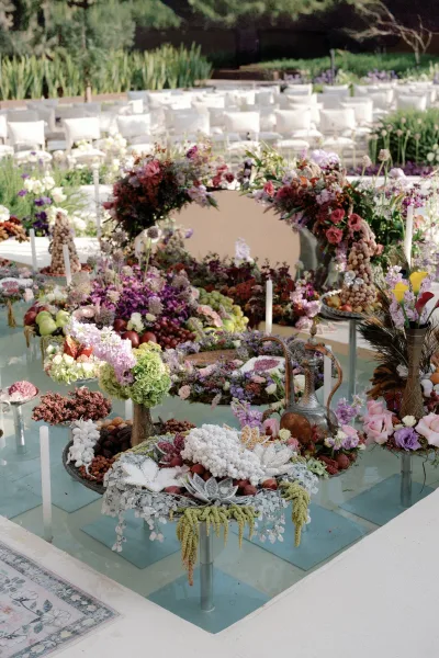 Wedding reception decor with wedding floral installation on glass floor platforms, pastel blooms and fruit, taper candles, set on a garden lawn
